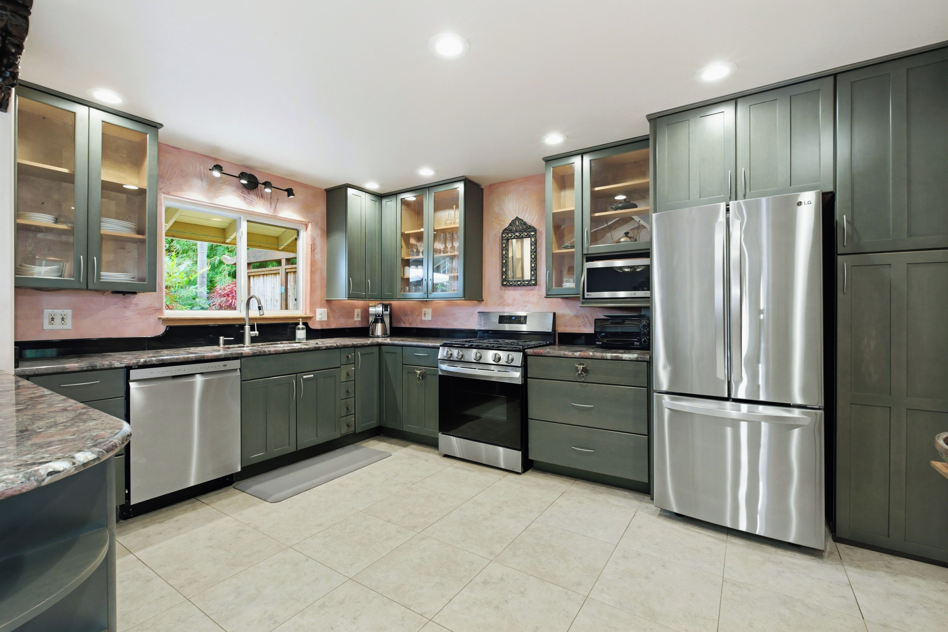 A modern kitchen with stainless steel appliances, green cabinets, and a large window.