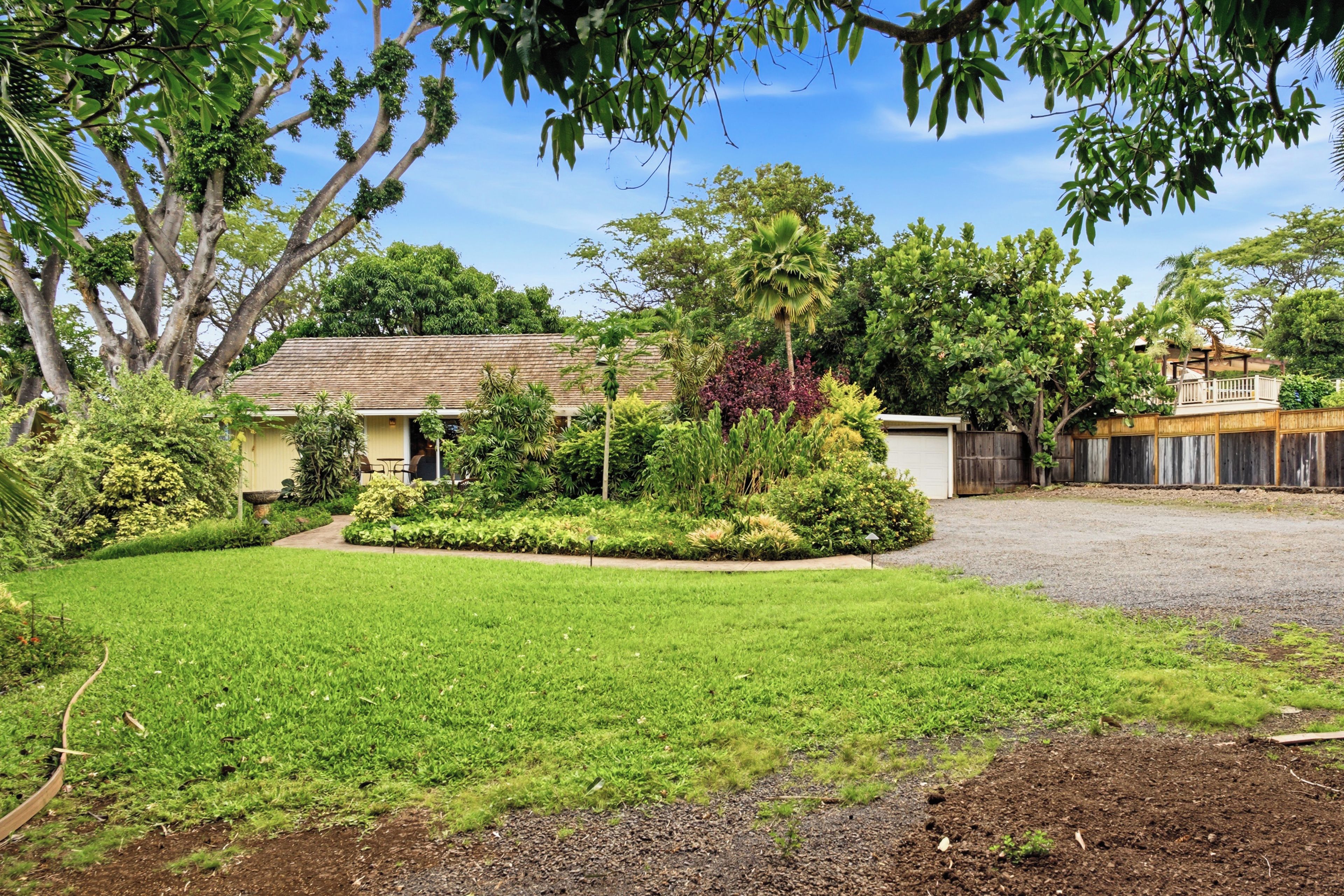 A residential property with a well-maintained lawn, a variety of plants, and a house with a tiled roof.