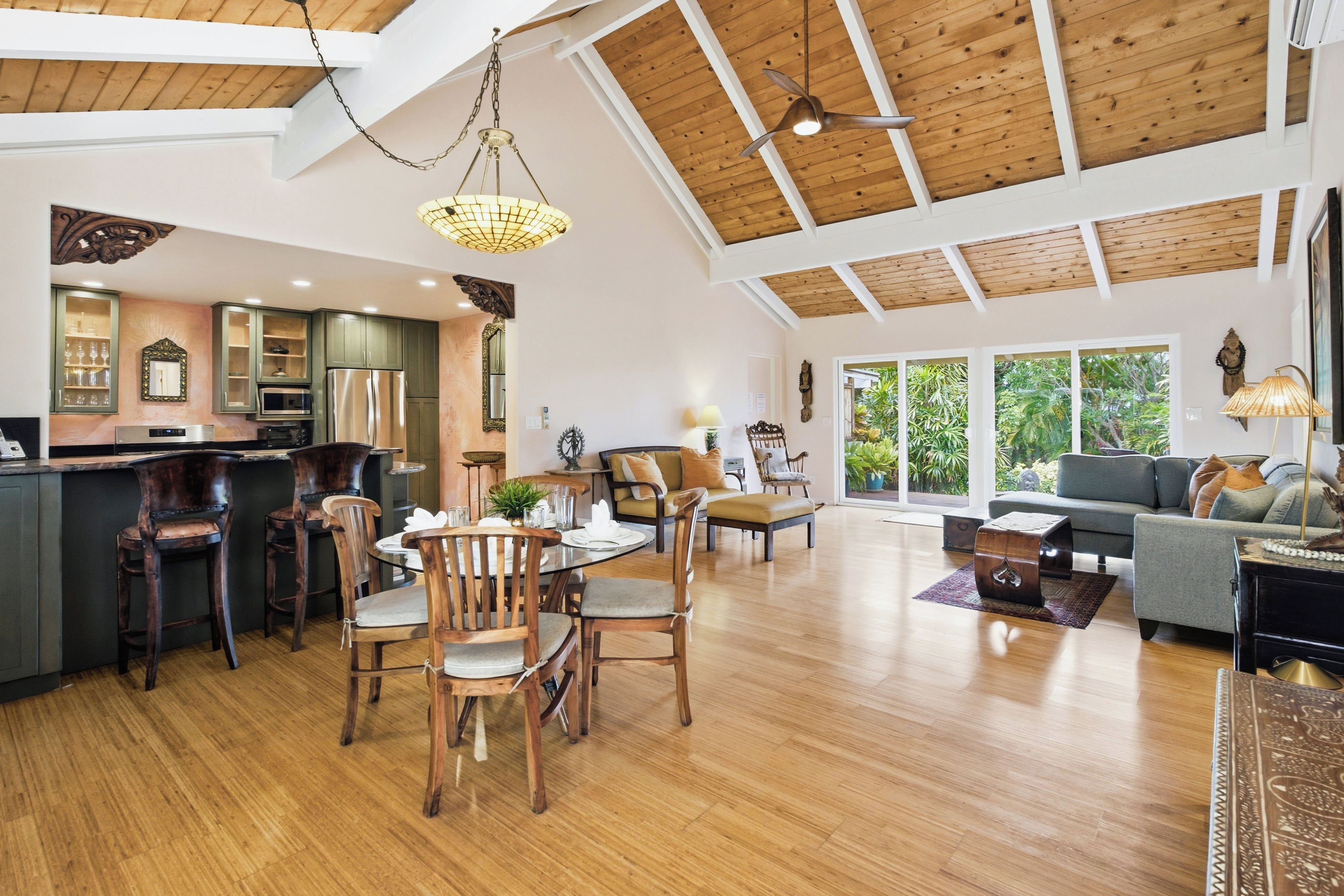 A spacious living area with a high ceiling, wooden beams, a dining area with wooden chairs and a table, and a kitchen with modern appliances.