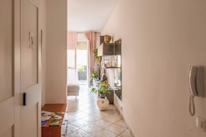 A hallway with a tiled floor, a wooden table with magazines, a potted plant, and a telephone on the wall. - B&B I Capperi (Lugo)