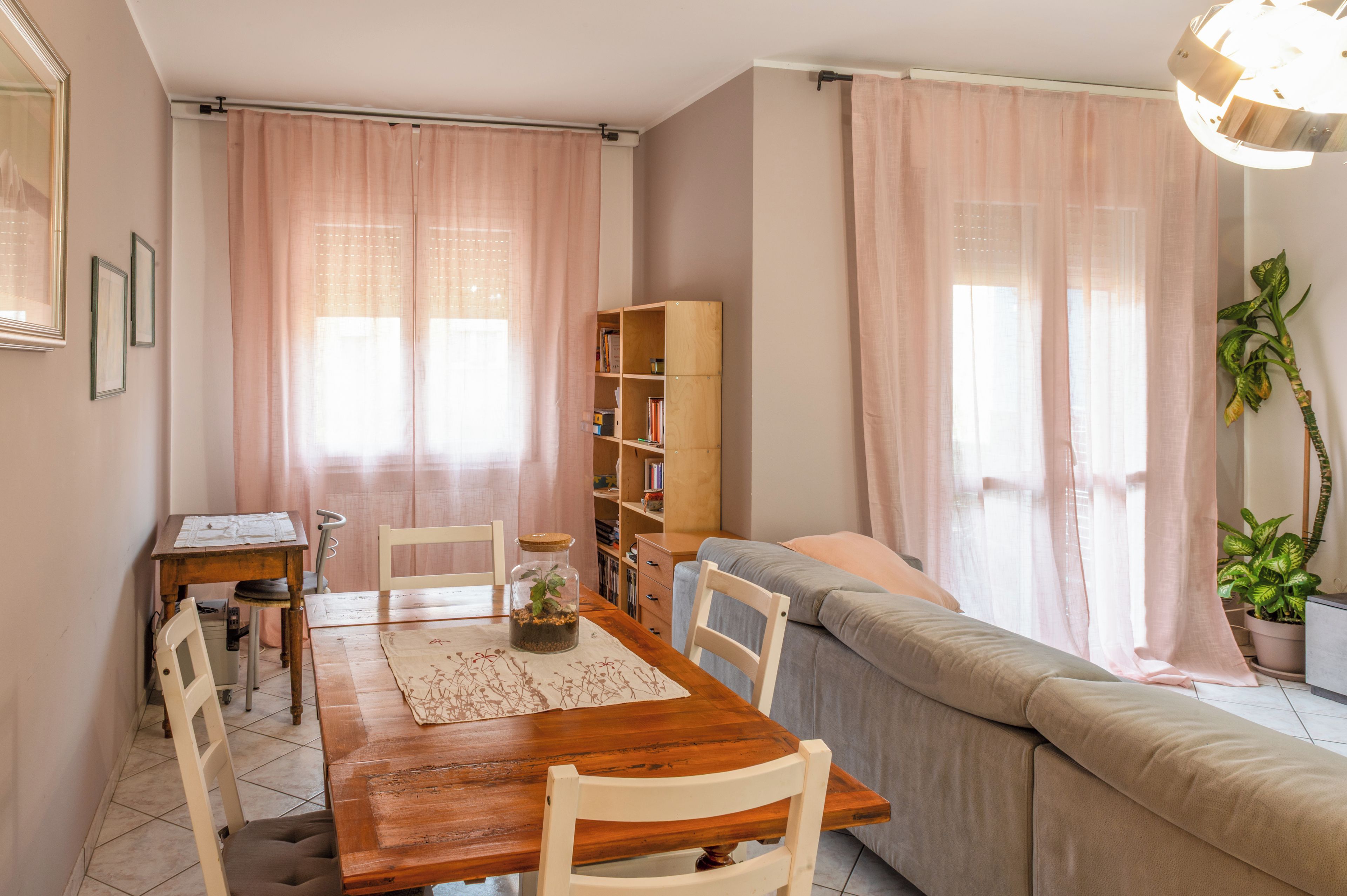 A cozy living room with a wooden dining table, chairs, a sofa, and a bookshelf.
