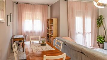A cozy living room with a wooden dining table, chairs, a sofa, and a bookshelf.