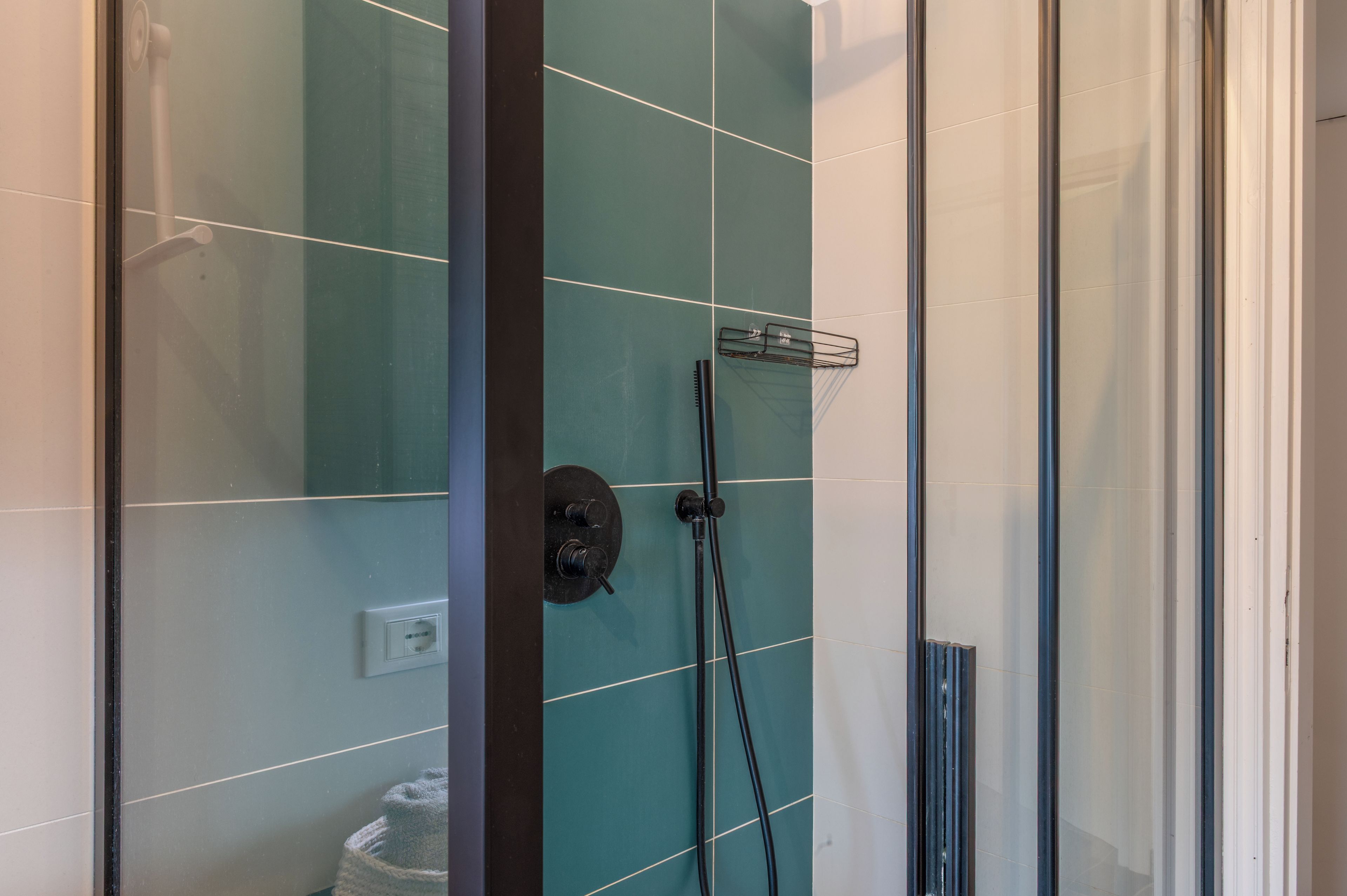 A glass-enclosed shower area with a control panel and a handheld showerhead.