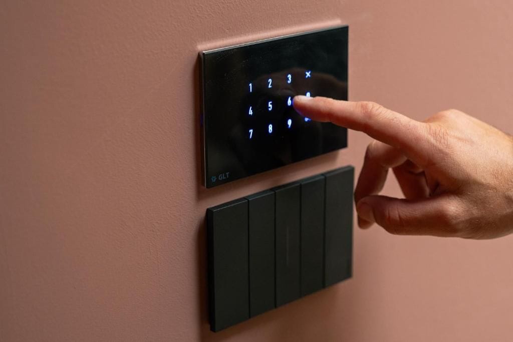 A hand pressing a button on a wall-mounted control panel with a keypad.