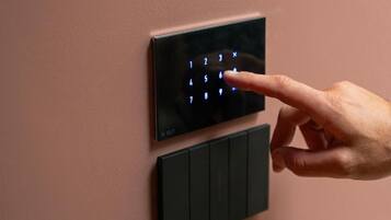 A hand pressing a button on a wall-mounted control panel with a keypad.
