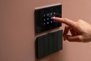 Une main appuyant sur un bouton situé sur un panneau de commande fixé au mur, panneau qui comporte également un clavier.