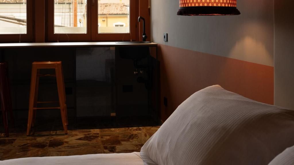 Una habitación con cama, un taburete, un lavabo y una ventana.
