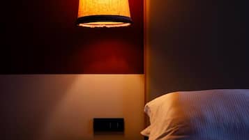A dimly lit room with a bed, a wall-mounted light fixture, and a power outlet.