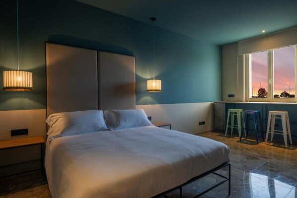 A bedroom with a bed, bedside tables, a window with a view, and a seating area with stools.