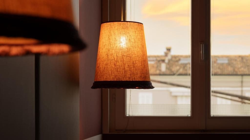 En lampa med en lampskärm med mönstrad yta, placerad nära ett fönster med utsikt över en bro.