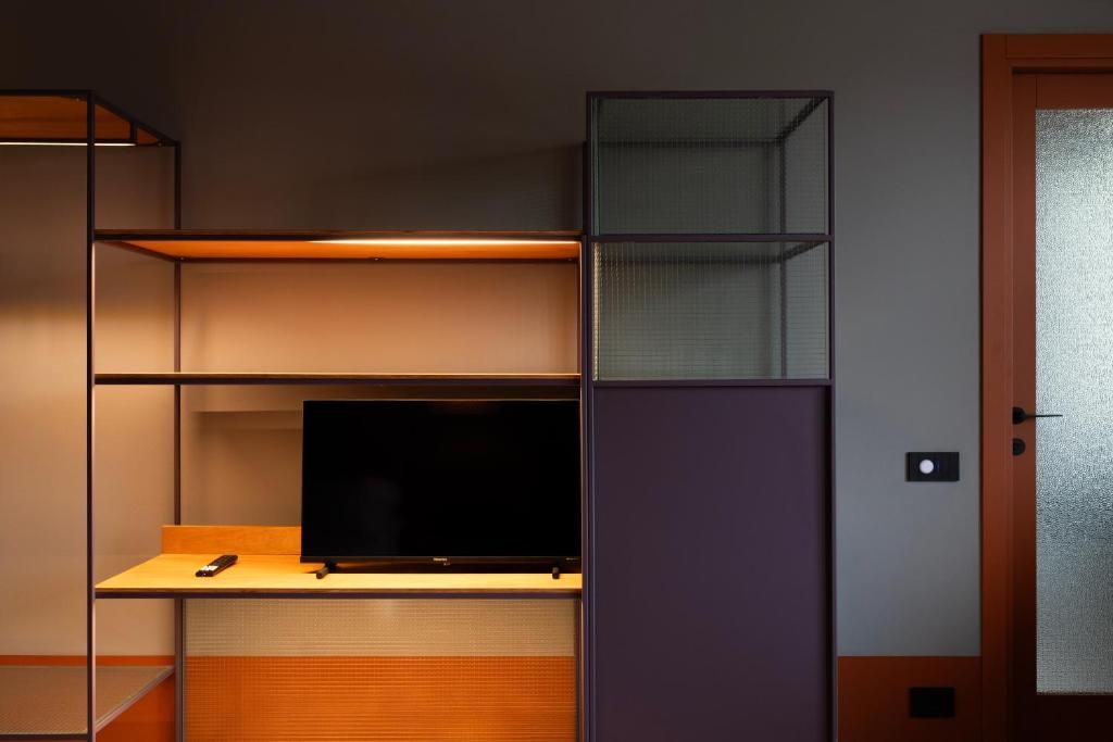 Una habitación con un televisor sobre una estantería de madera, una puerta con un panel de vidrio esmerilado y una lámpara fijada a la pared.
