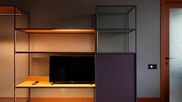 Una habitación con un televisor sobre una estantería de madera, una puerta con un panel de vidrio esmerilado y una lámpara fijada a la pared.
