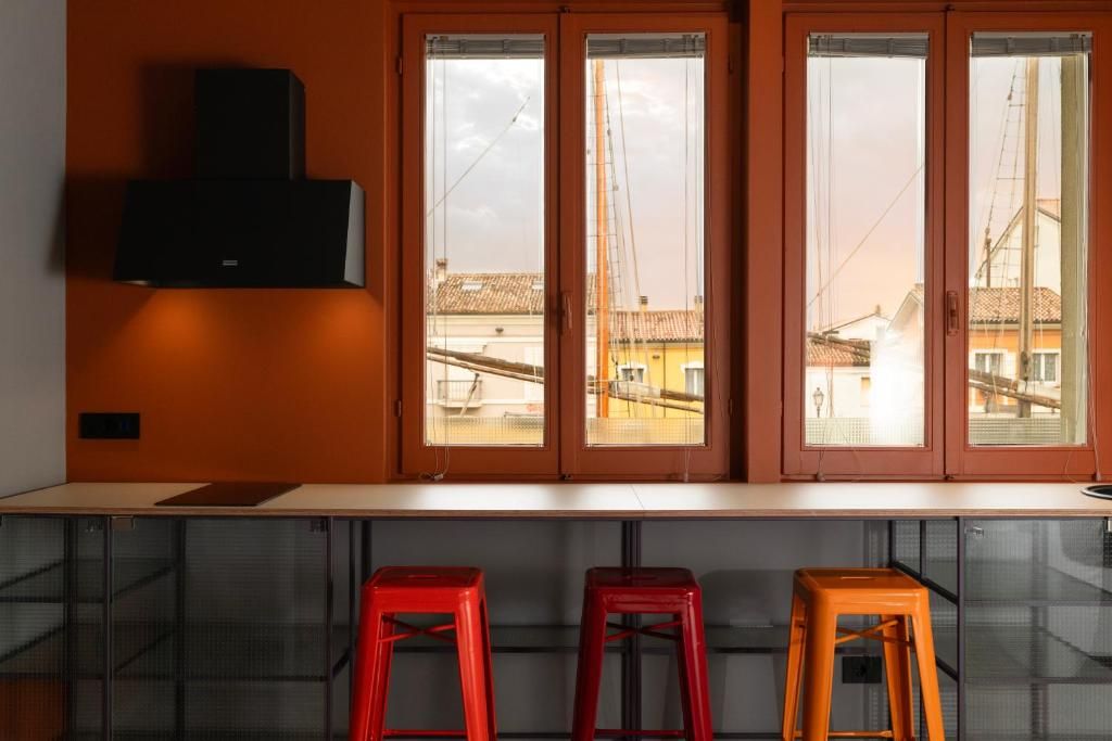 A kitchen with a built-in stove, three stools, and a window with a view of buildings.