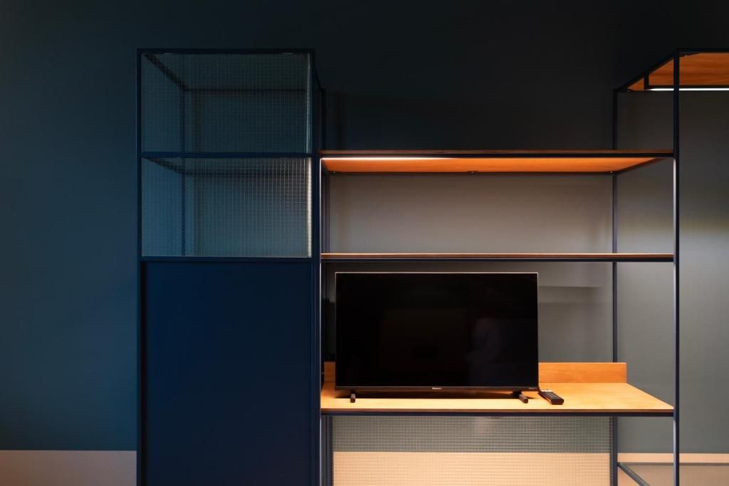 A room with a dark blue wall, a wooden desk with a flat-screen TV, and a metal shelving unit.