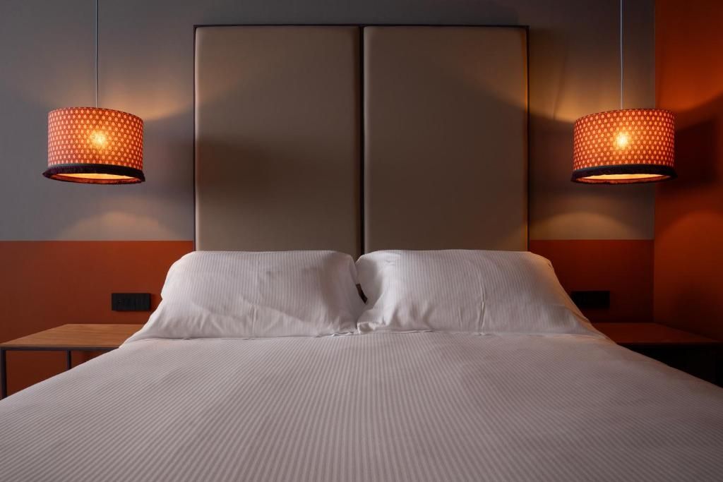 A hotel room with a large bed, two nightstands, and two wall-mounted lamps.