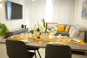 Een eethoek met een tafel voor vier personen, met een vaas met bloemen, wijnflessen en een moderne flatscreen televisie aan de muur.