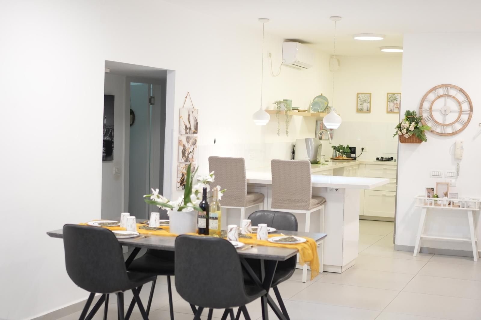 Een moderne eetruimte met een tafel gedekt voor twee personen, stoelen en een keuken op de achtergrond.