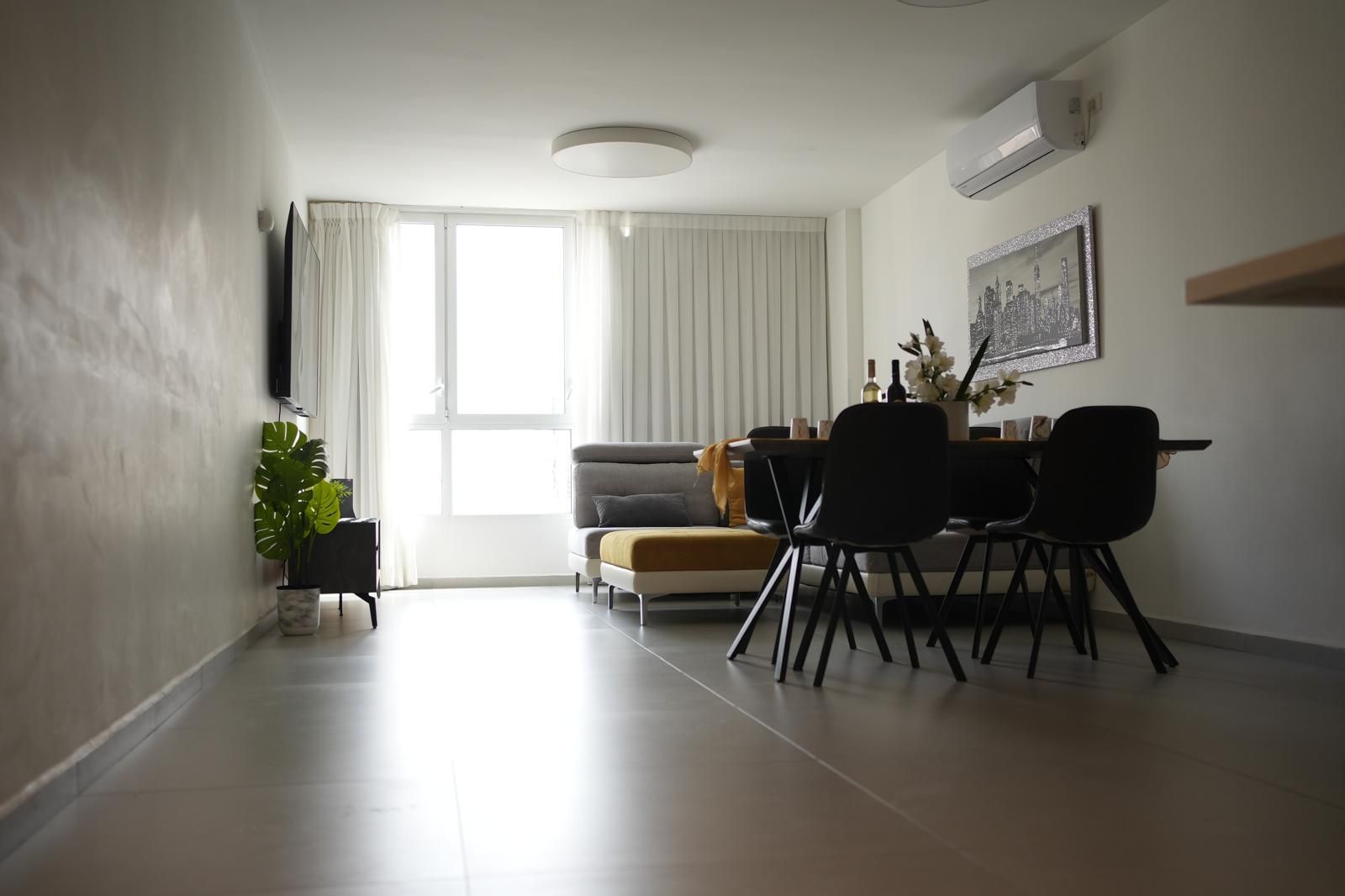 Una sala de estar moderna con un sofá, una mesa de comedor, sillas y una planta en maceta.