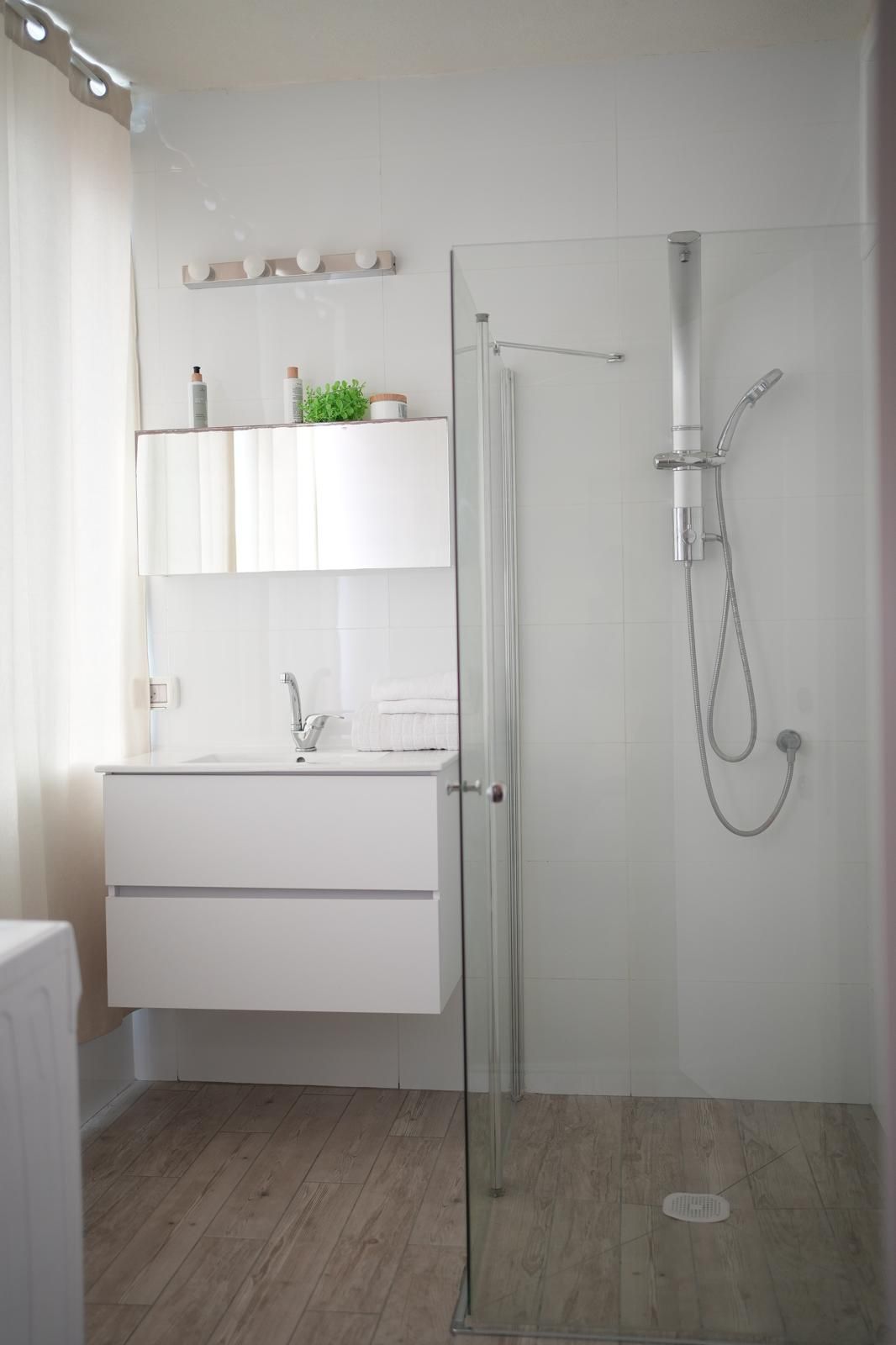 A modern bathroom with a glass shower enclosure, a white vanity with a sink, and a mirror above the vanity.