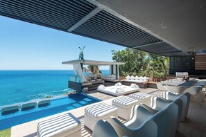 A poolside area with a view of the ocean, outdoor seating, and a bar area.