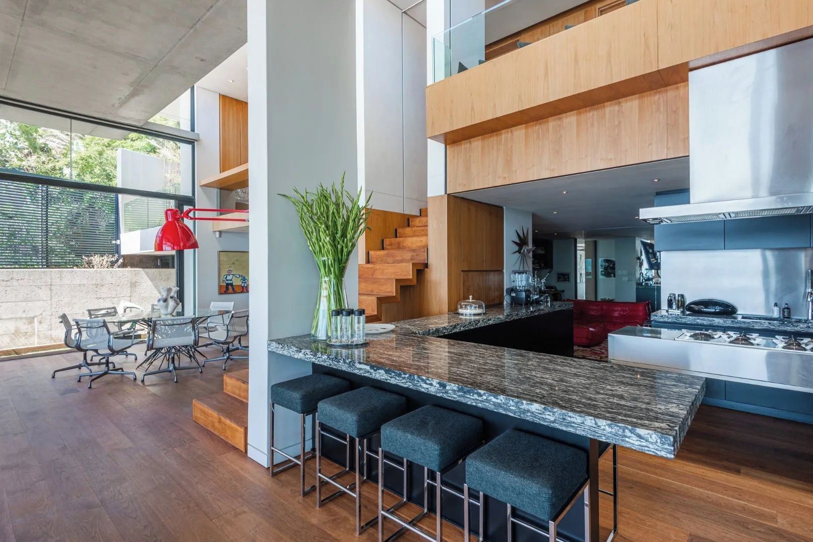 A modern kitchen with a marble countertop, bar stools, and a red pendant light.