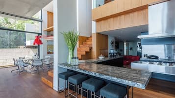 A modern kitchen with a marble countertop, bar stools, and a red pendant light.