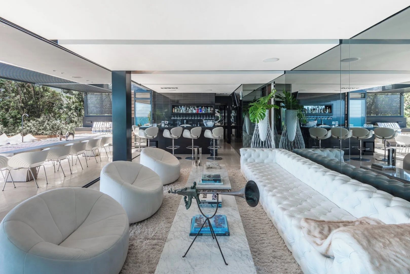 A modern lounge area with white sofas, bar stools, and a bar with a variety of bottles.