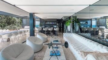A modern lounge area with white sofas, bar stools, and a bar with a variety of bottles.
