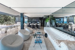 Un espace lounge moderne avec des canapés blancs, des tabourets de bar et un bar proposant une grande variété de bouteilles.