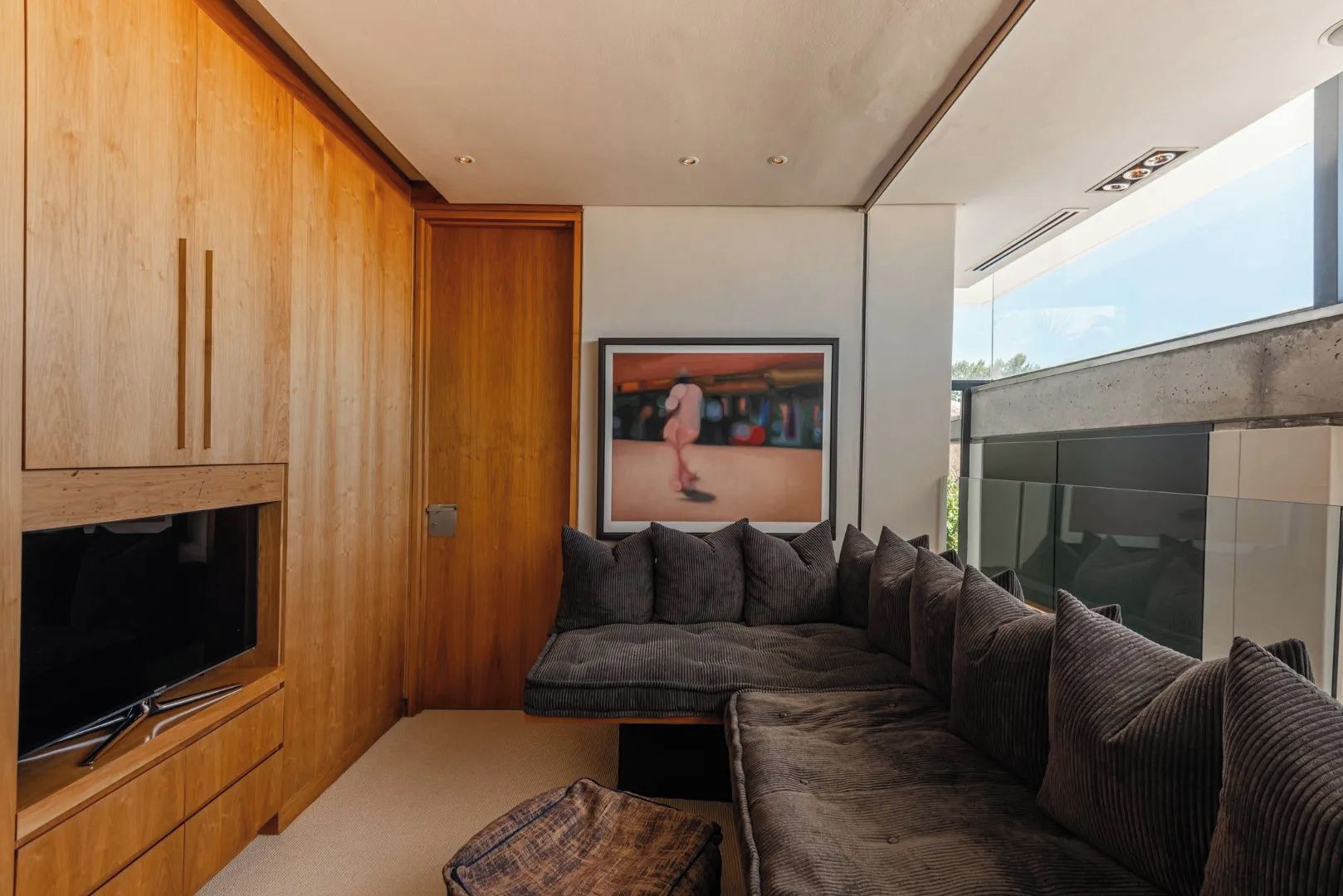 A modern living room with a large sectional sofa, a flat-screen TV, wooden cabinetry, and a large window.