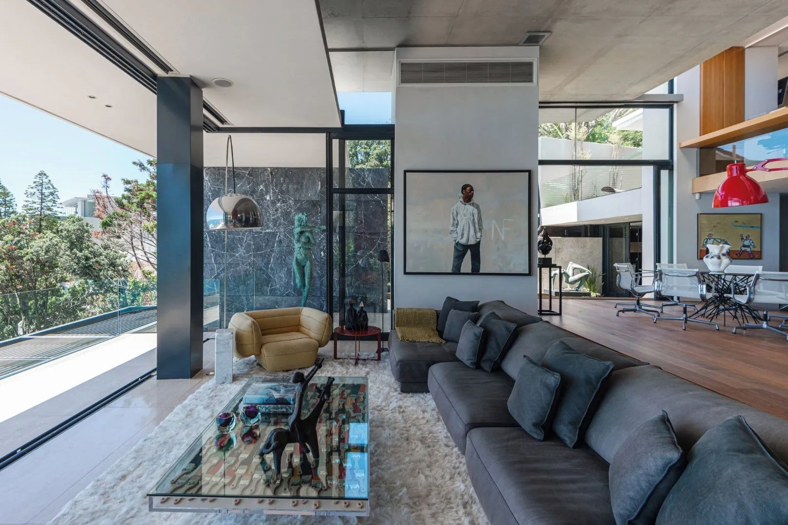 A modern living room with a large sofa, a coffee table with decorative items, a painting, and a view of the outdoors.