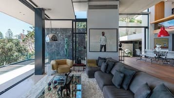 A modern living room with a large sofa, a coffee table with decorative items, a painting, and a view of the outdoors.