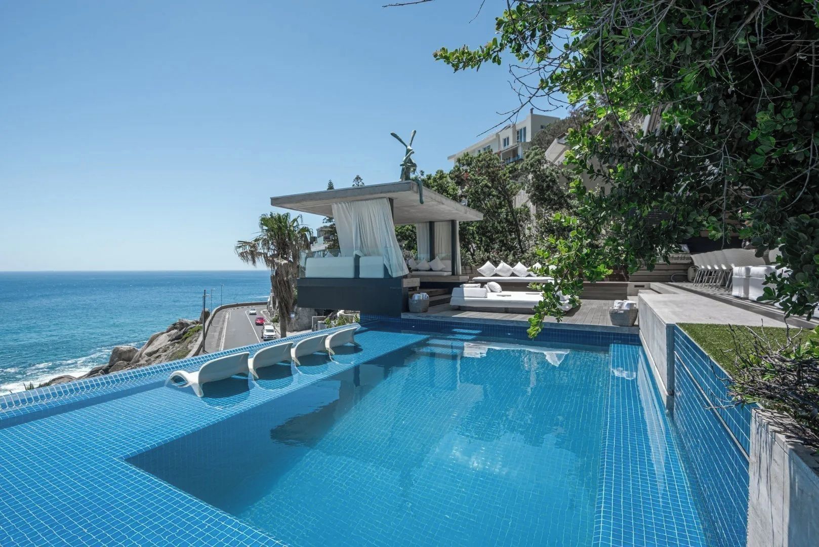Ein Pool mit Blick aufs Meer, ein überdachter Sitzbereich und ein Gebäude im Hintergrund.