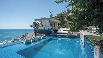 Ein Pool mit Blick aufs Meer, ein überdachter Sitzbereich und ein Gebäude im Hintergrund.