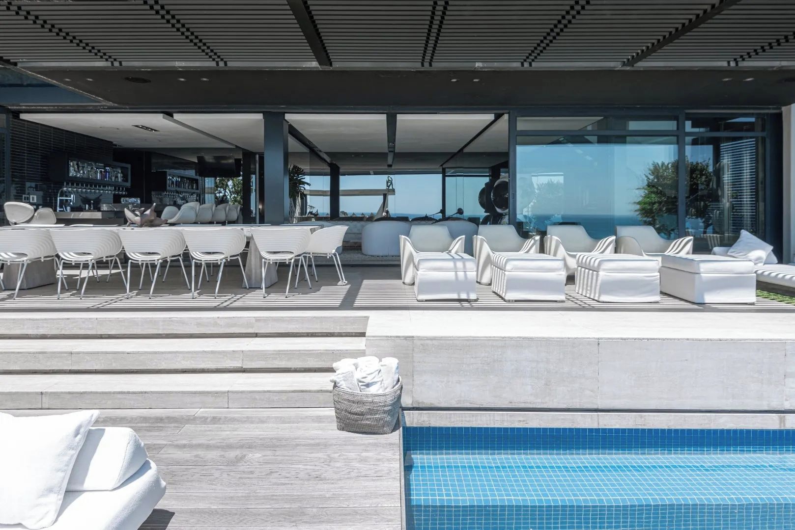 Un espace piscine extérieur moderne, doté de chaises longues et d’un bar.