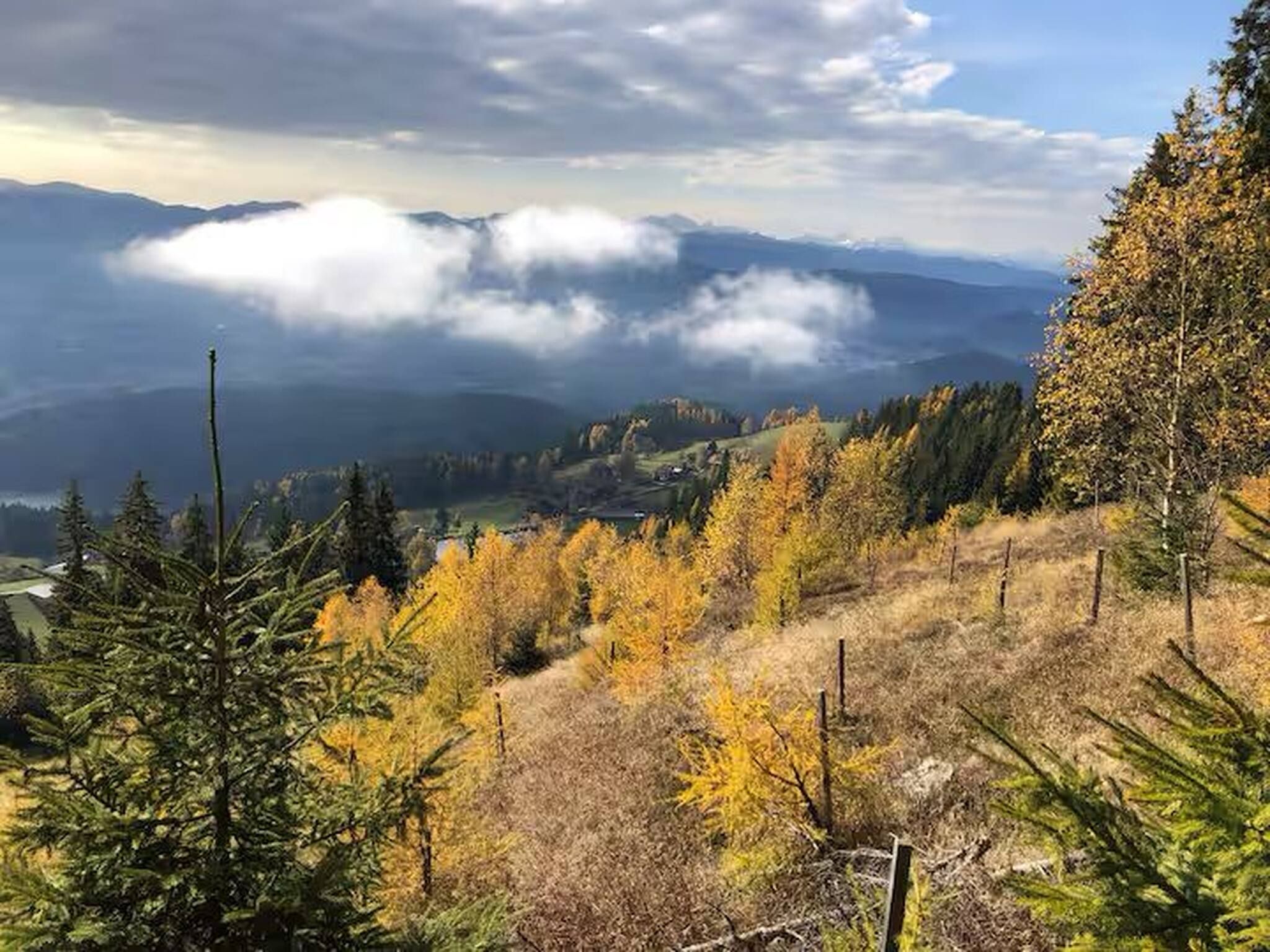 Un paysage montagneux aux couleurs automnales, avec un ciel dégagé et des nuages à l’horizon.
