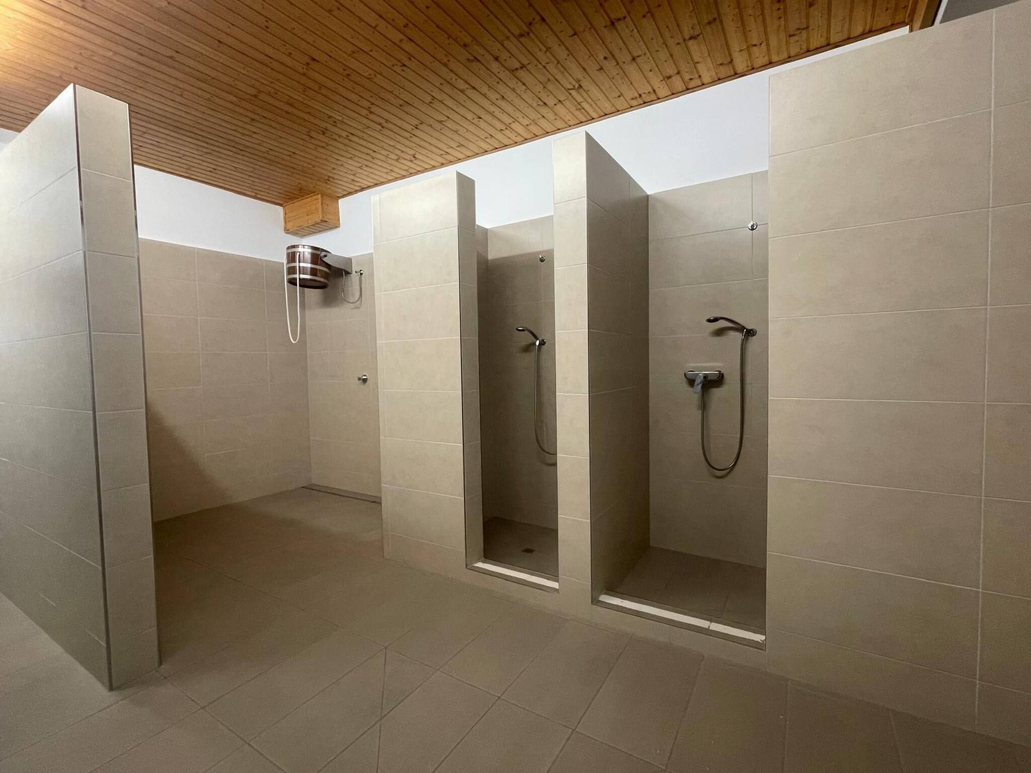 Ein modernes Badezimmer mit drei Duschkabinen, Holzboden und gefliesten Wänden.