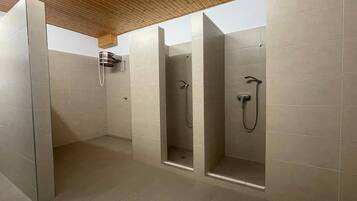 Ein modernes Badezimmer mit drei Duschkabinen, Holzboden und gefliesten Wänden.