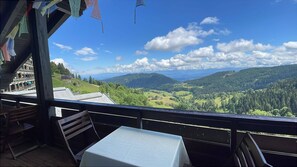 Ein Balkon mit Tisch und Stühlen, der auf eine gebirgige Landschaft mit blauem Himmel blickt.
