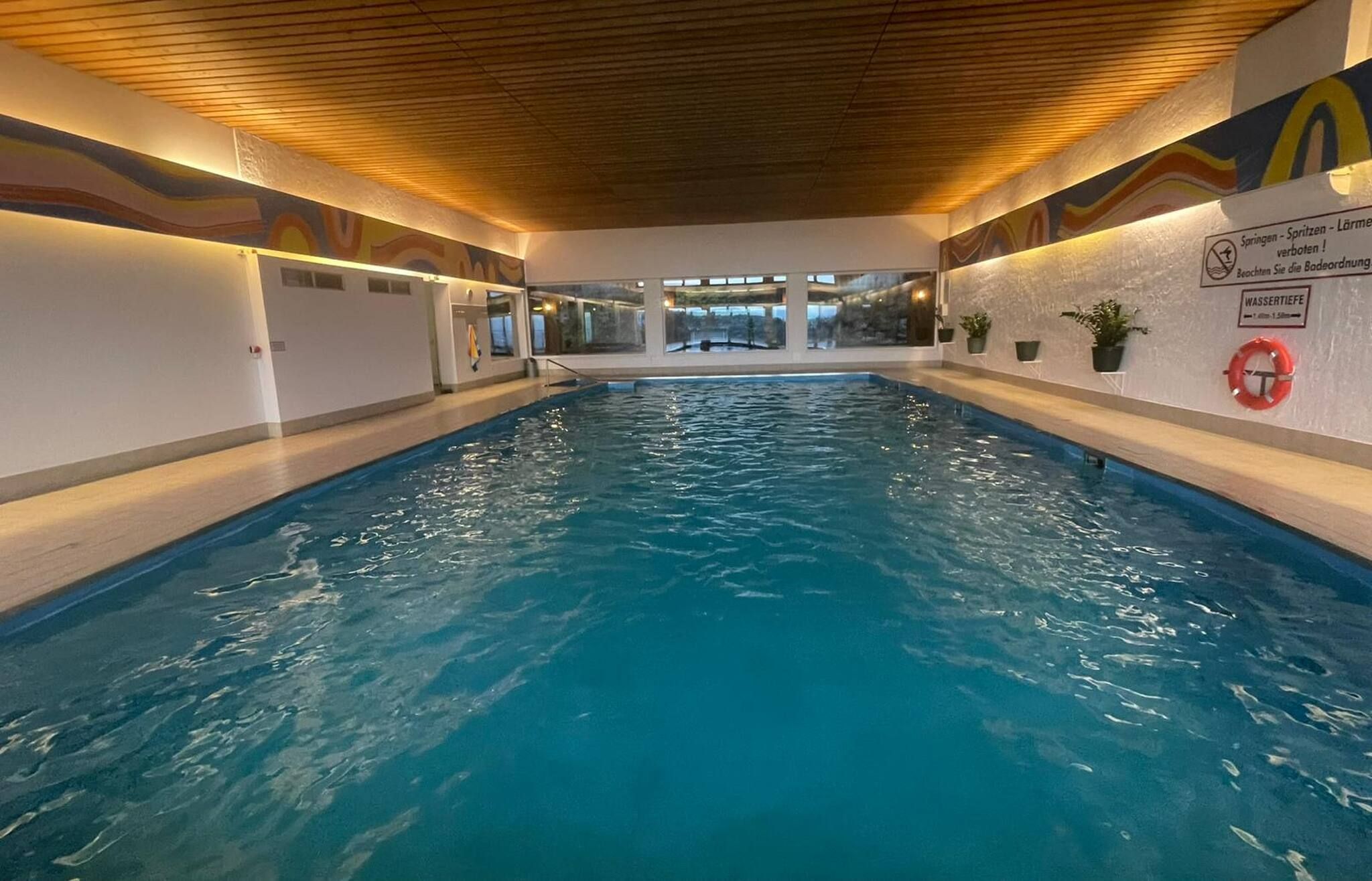 An indoor swimming pool with clear water, wooden ceiling, and walls with safety signs.