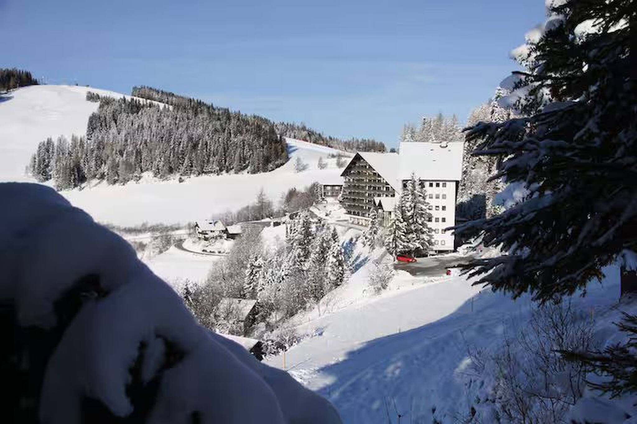 Un paisaje montañoso cubierto de nieve con una cabaña y un edificio de techo inclinado.