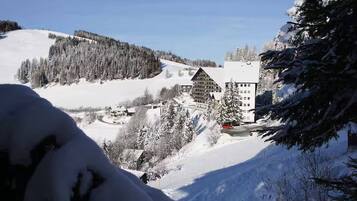 Un paisaje montañoso cubierto de nieve con una cabaña y un edificio de techo inclinado.