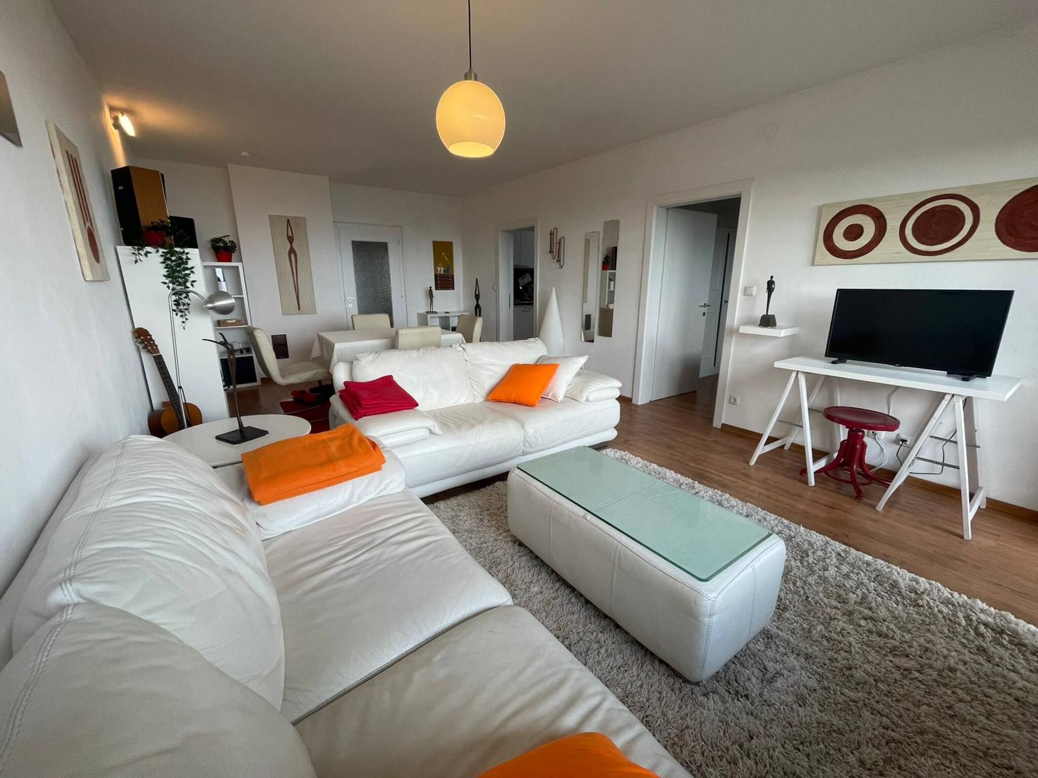Ein modernes Wohnzimmer mit einem weißen Sofa, einem Glastisch und einem Fernsehgerät auf einer weißen Ablagefläche.