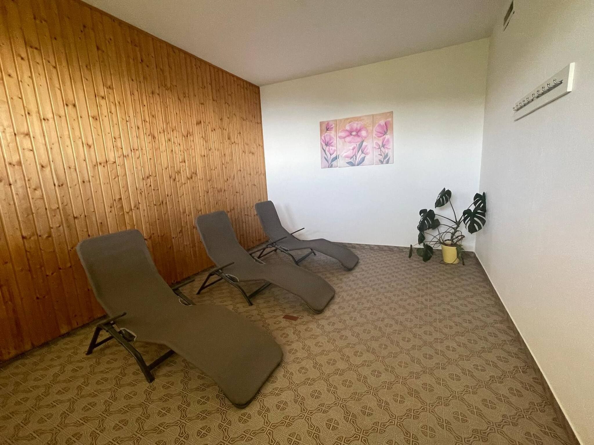 Ein Zimmer mit drei Liegesesseln, einer Holzwand, einem Blumenbild und einem Blumentopf.