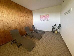 Ein Zimmer mit drei Liegesesseln, einer Holzwand, einem Blumenbild und einem Blumentopf.