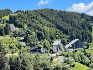 Eine gebirgige Landschaft mit einer Ansammlung von Gebäuden, darunter ein großes Mehrstöckiges Hotel und ein kleineres Gebäude in der Nähe.