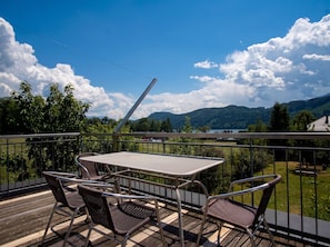 A balcony with a table and chairs, overlooking a lake and mountains. - Lichtblick Panorama · Balcony with a Lake View · Peace and Quiet (Seeboden)
