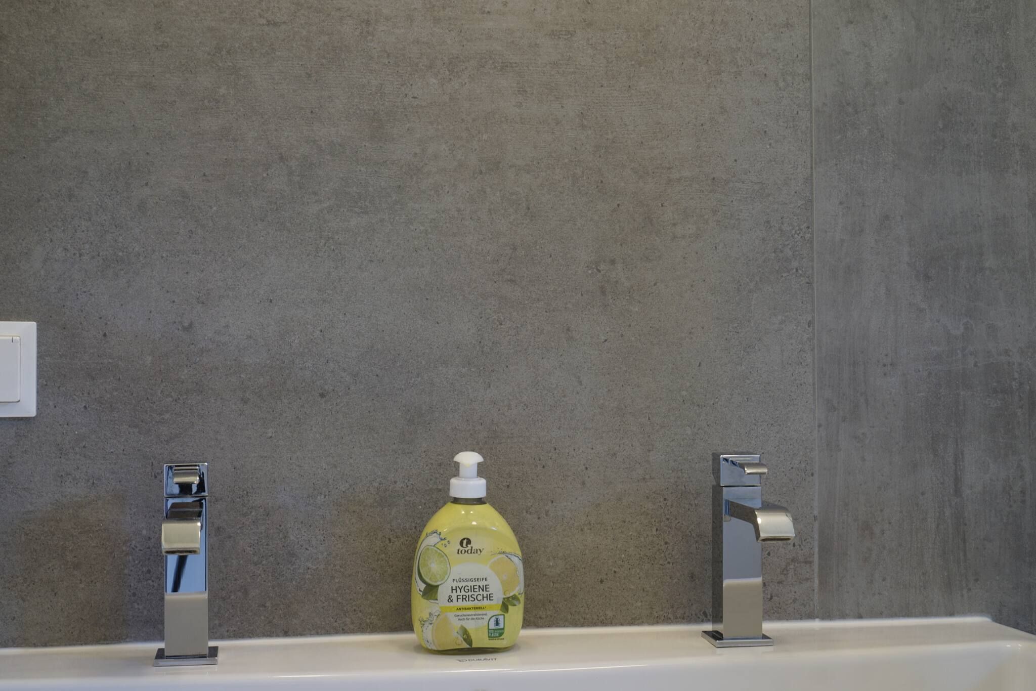 Een badkamer met een wastafel, twee kraanpunten en een fles vloeibare zeep.