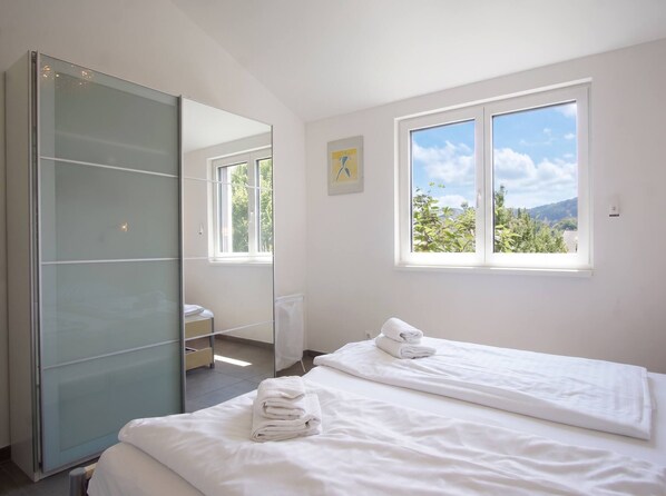 Een hotelkamer met een bed, een grote spiegel, een raam met uitzicht op groen en een kunstwerk aan de muur.