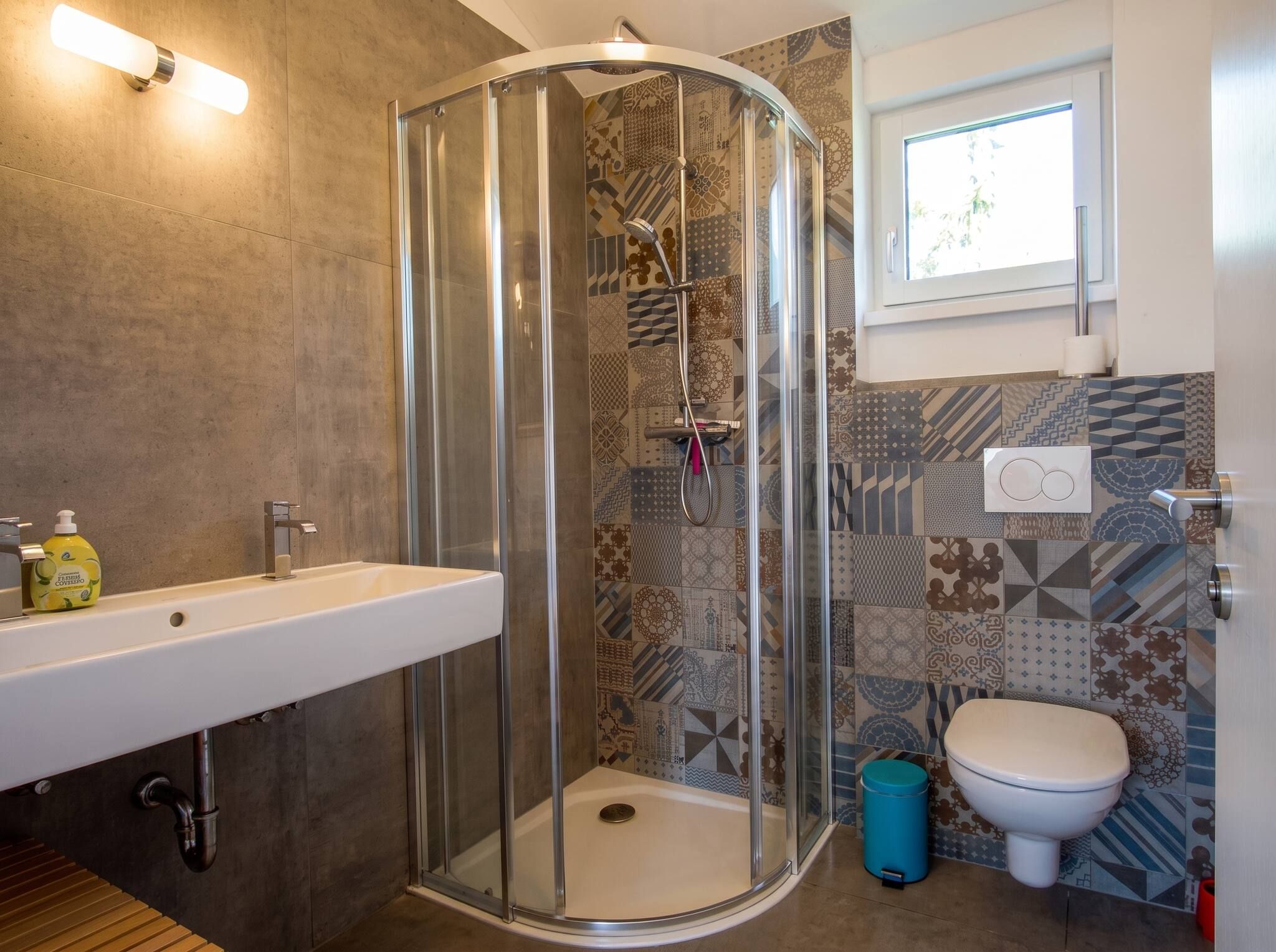 A bathroom with a glass-enclosed shower, a white sink, a toilet, and patterned tiles.
